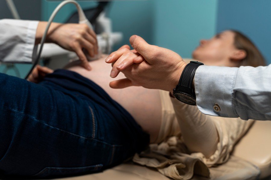 Pregnant woman undergoing an ultrasound examination while a healthcare professional examines her abdomen.