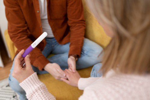 Infertility Treatment consultation with a woman holding a pregnancy test while discussing fertility and family planning with her partner