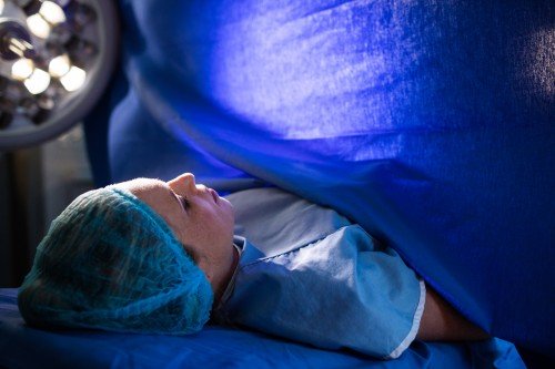 Pregnant woman prepared for Cesarean Delivery lying on an operating table under a blue surgical drape in a hospital operating room.